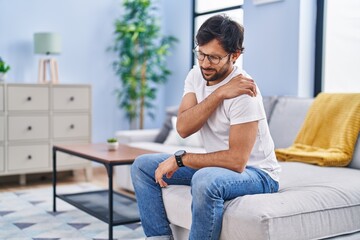 Young hispanic man suffering for back ache sitting on sofa at home