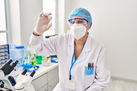 Middle age woman wearing scientist unifor and medical mask holding dose vaccine at laboratory