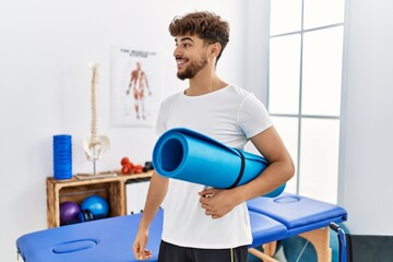 Young arab man patient smiling confident holding yoga mat at clinic