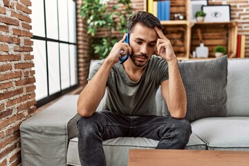 Young hispanic man worried talking on the smartphone at home