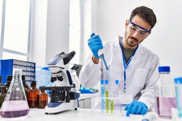 Young hispanic man wearing scientist uniform using pipette at laboratory
