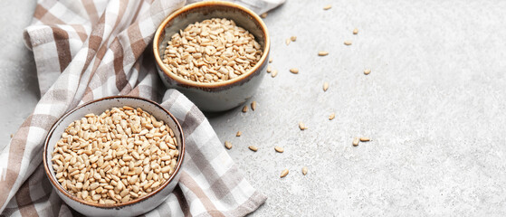 Bowls with peeled sunflower seeds on light background with space for text