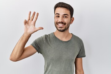 Fototapeta premium Young hispanic man with beard wearing casual t shirt over white background showing and pointing up with fingers number four while smiling confident and happy.