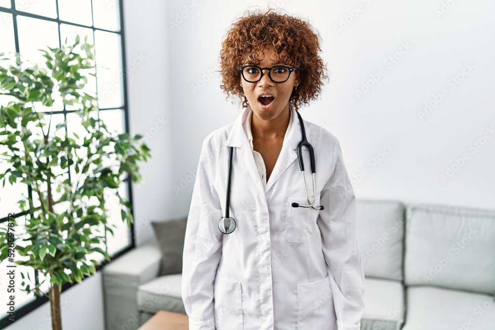 Sticker young african american woman wearing doctor uniform and stethoscope afraid and shocked with surprise