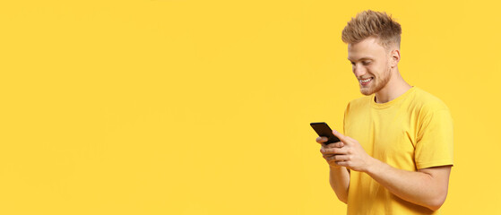 Portrait of happy young man with mobile phone on yellow background with space for text