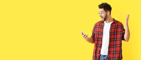 Surprised young man with mobile phone on yellow background with space for text