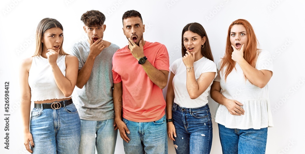 Poster group of young friends standing together over isolated background looking fascinated with disbelief,