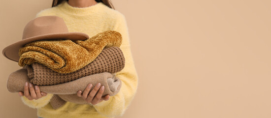 Woman holding stack of warm sweaters and felt hat on color background with space for text