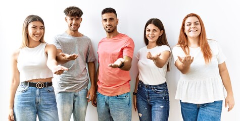 Obraz premium Group of young friends standing together over isolated background smiling cheerful offering palm hand giving assistance and acceptance.