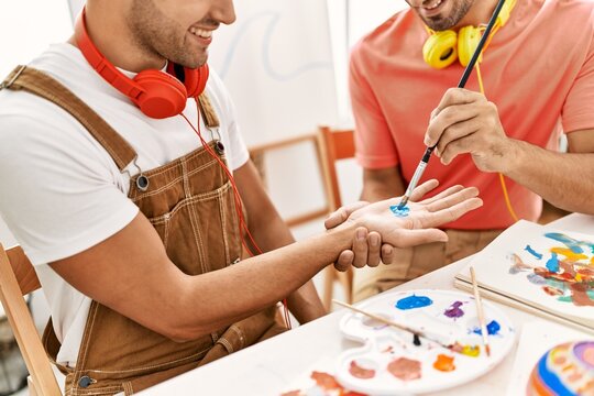 Two hispanic men couple smiling confident painting palm hands at art studio