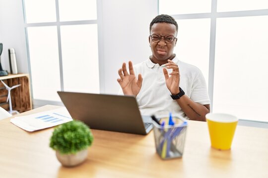Young african man working at the office using computer laptop disgusted expression, displeased and fearful doing disgust face because aversion reaction.