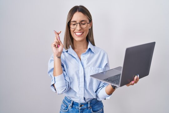 Young woman working using computer laptop gesturing finger crossed smiling with hope and eyes closed. luck and superstitious concept.
