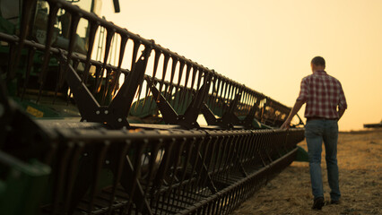 Rancher check field thresher reel farming vehicle at golden sunset countryside.