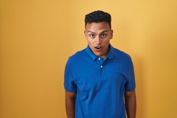 Young hispanic man standing over yellow background afraid and shocked with surprise and amazed expression, fear and excited face.