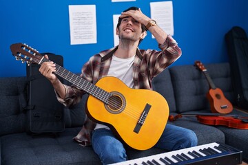 Obraz premium Young hispanic man playing classic guitar at music studio stressed and frustrated with hand on head, surprised and angry face