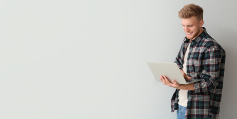 Handsome young man with laptop on light background with space for text