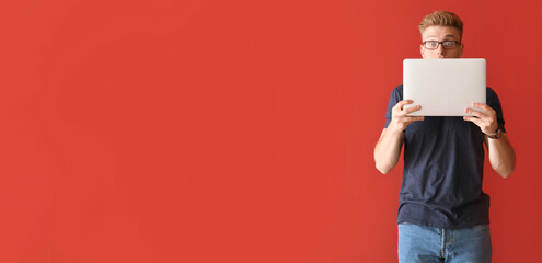 Shocked young man with laptop on red background with space for text