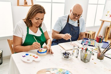 Obraz na płótnie Canvas Middle age hispanic painter couple smiling happy painting at art studio.