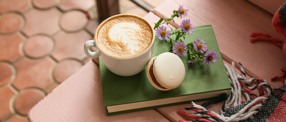 Cup of tasty coffee, macaron and notebook on table in cafe