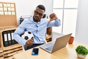 Young african man football hooligan cheering game at the office with angry face, negative sign showing dislike with thumbs down, rejection concept