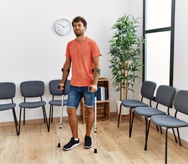 Fototapeta na wymiar Young hispanic man walking using crutches at clinic waiting room.