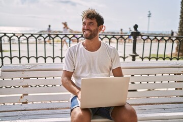 Young hispanic man smiling confident using laptop at seaside