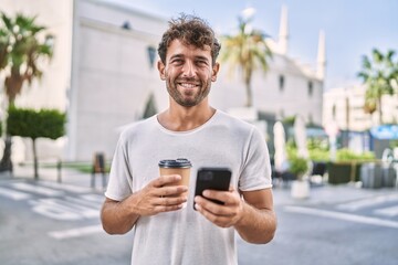Young hispanic man using smartphone drinking coffee at street