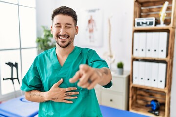 Fototapeta premium Young physiotherapist man working at pain recovery clinic laughing at you, pointing finger to the camera with hand over body, shame expression