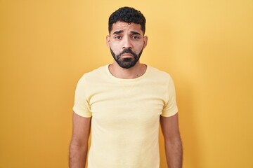 Hispanic man with beard standing over yellow background depressed and worry for distress, crying...