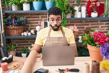 Hispanic man with beard working at florist shop doing video call scared and amazed with open mouth for surprise, disbelief face