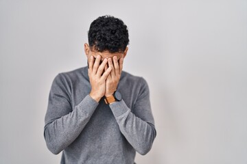 Hispanic man with beard standing over white background with sad expression covering face with hands...