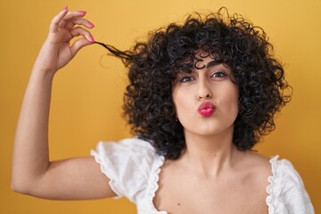Young brunette woman with curly hair holding curl looking at the camera blowing a kiss being lovely...