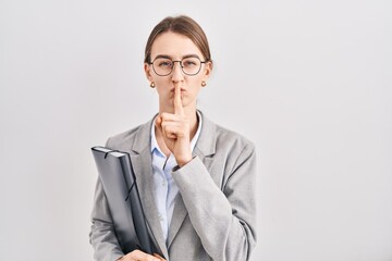 Young caucasian woman wearing business clothes and glasses asking to be quiet with finger on lips....