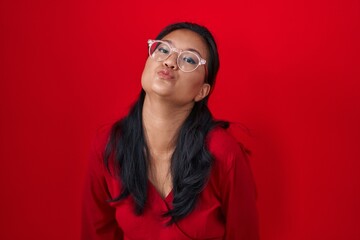Asian young woman standing over red background looking at the camera blowing a kiss on air being lovely and sexy. love expression.