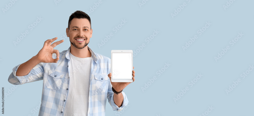Poster handsome man holding tablet computer and showing ok on light blue background with space for text