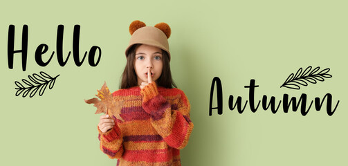 Cute little girl with autumn leaf showing silence gesture on green background