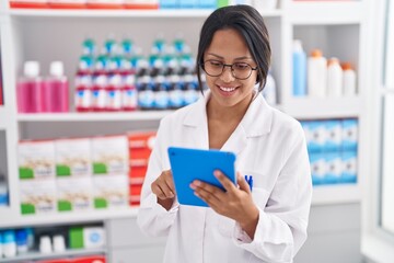 Young hispanic woman pharmacist using touchpad working at pharmacy