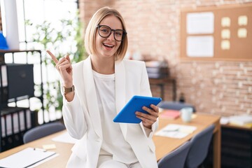Young caucasian woman working at the office wearing glasses with a big smile on face, pointing with...