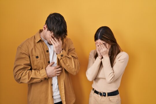Young hispanic couple standing over yellow background with sad expression covering face with hands while crying. depression concept.