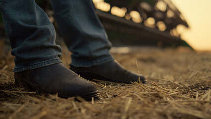 Agronomist boots stand field at harvester straw closeup. Sunset countryside
