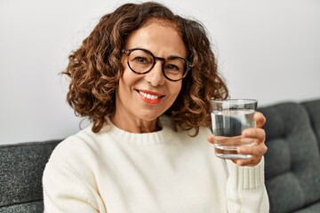 Middle age hispanic woman smiling confident drinking water at home