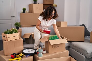 Middle age hispanic woman packing boxes at new home