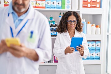 Man and woman pharmacists using touchpad and smartphone working at pharmacy