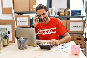 Handsome hispanic man working as volunteer doing countability speaking on the phone at donation stand