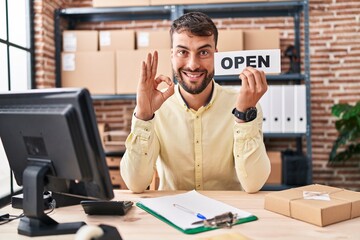 Handsome hispanic man working at small business ecommerce doing ok sign with fingers, smiling friendly gesturing excellent symbol