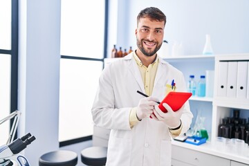 Young hispanic man wearing scientist uniform using touchpad at laboratory