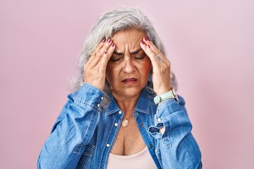 Middle age woman with grey hair standing over pink background with hand on head, headache because stress. suffering migraine.