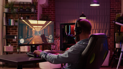 Man using pc gaming setup relaxing playing multiplayer online action game talking to team on...