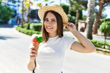 Young beautiful woman smiling happy outdoors on a sunny day wearing a summer hat and eating ice cream