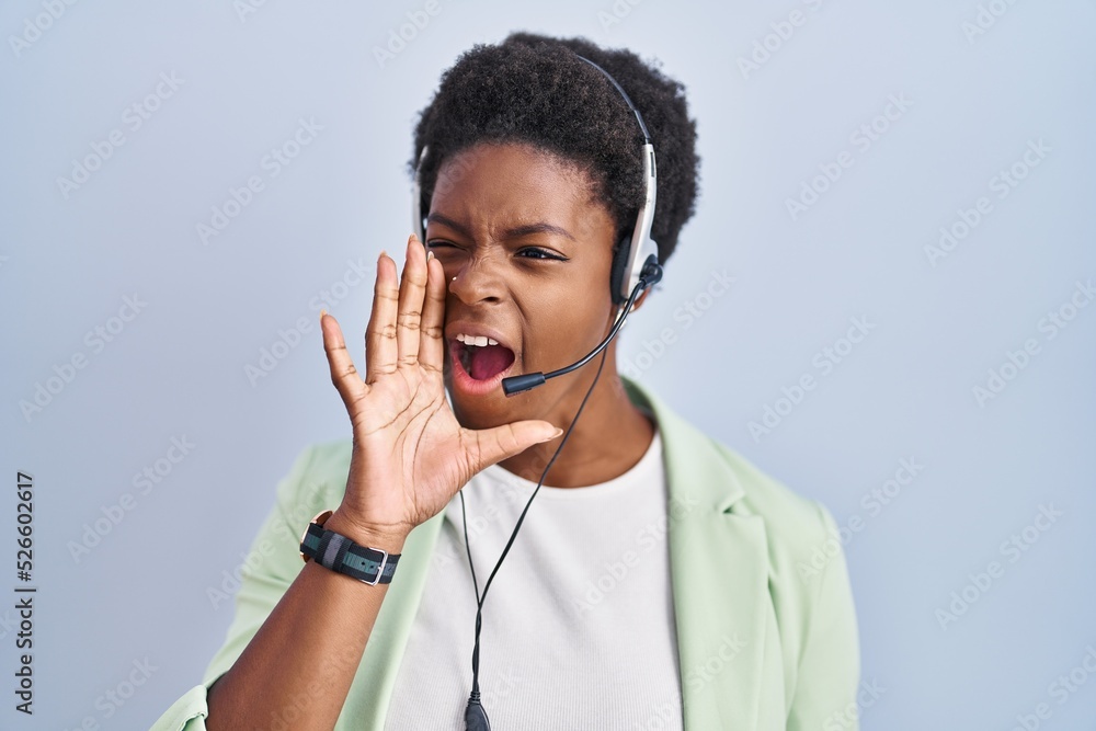 Wall mural African american woman wearing call center agent headset shouting and screaming loud to side with hand on mouth. communication concept.